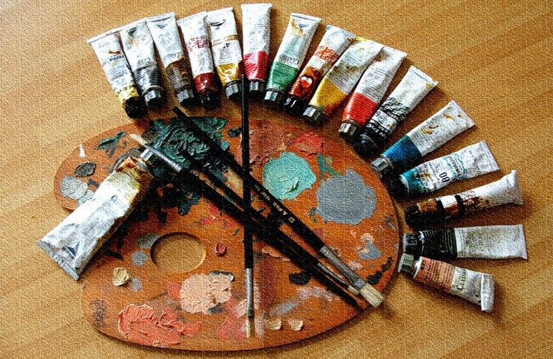 An oil painting artists palette with tubes of paint and three different paint brushes